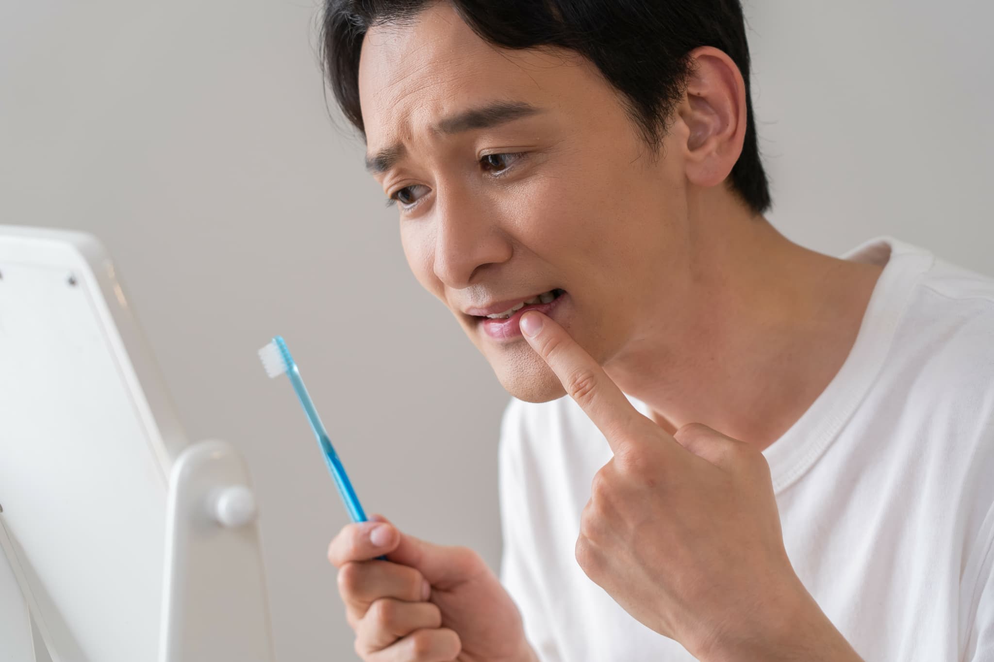 歯周病の進行が気になり鏡で歯ぐきを見ている男性