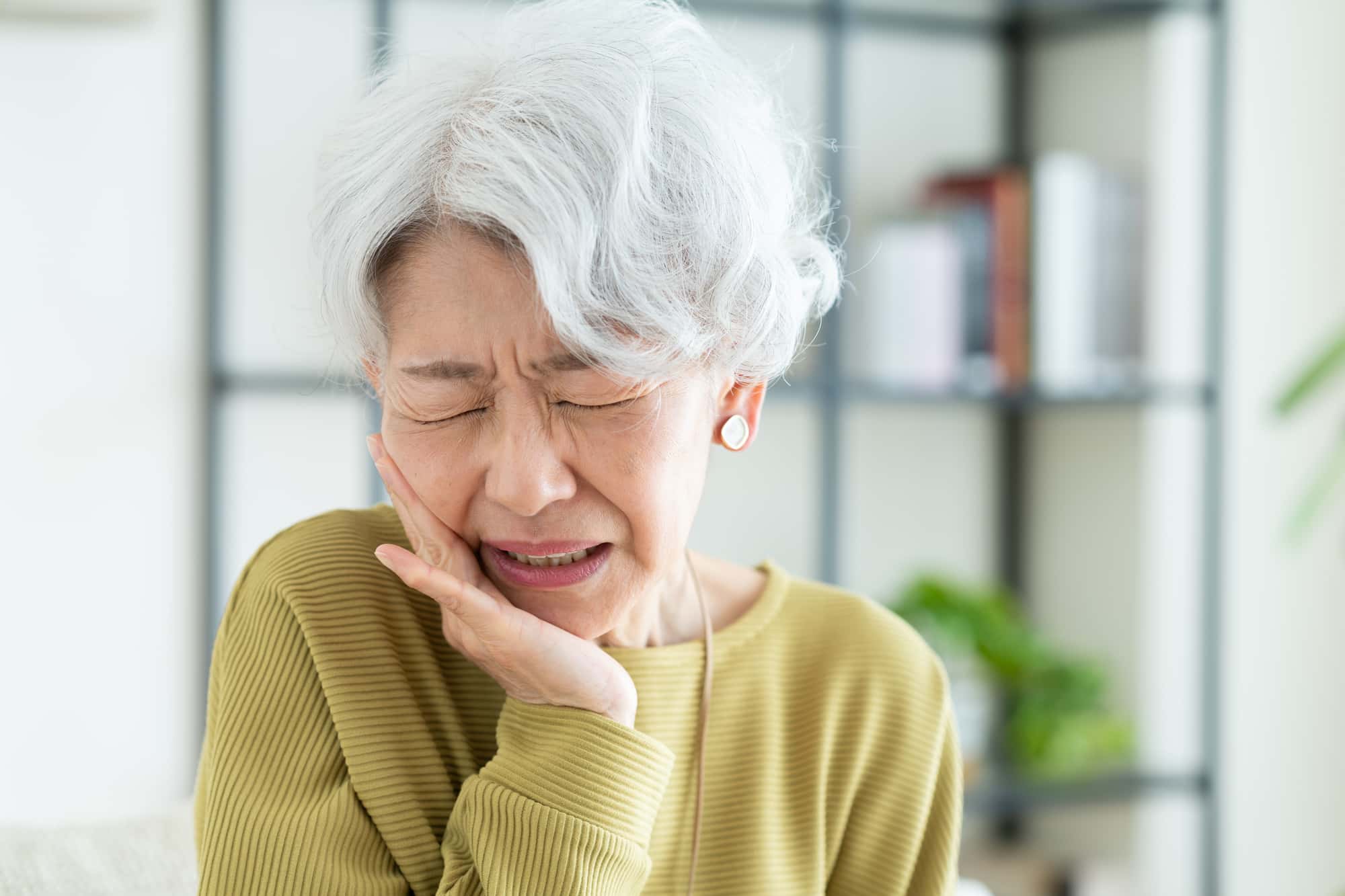 インプラントの抜歯後に痛む頬を押さえる女性