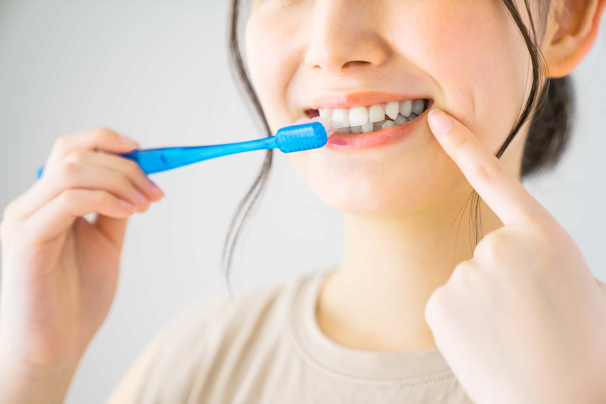 歯周病が重度に進行するのを防ぐためにしっかり歯磨きをしていることを指さしてアピールする女性